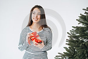 Portrait of young smiling asian woman with gift box in hands with Christmas tree on white background isolated