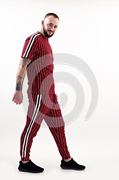 Portrait of young smiling bearded man with short dark hair wearing red striped sport wear, standing on white background.