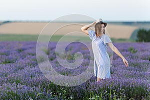 Portrait of young smiling beautiful woman in blue dress, hat on purple lavender flower blossom meadow field outdoors on
