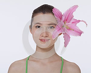 Portrait of young, smiling, beautiful woman with a large pink flower tucked behind her ear, studio shot