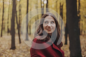 Portrait of young smiling beautiful woman wearing coat in autumn forest