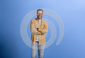 Portrait of young smiling businessman with arms crossed posing confidently over blue background