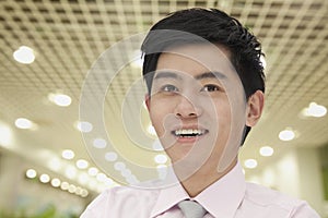 Portrait of young smiling businessman indoors with rows of lights