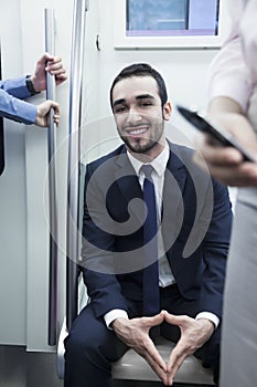 Portrait of young smiling businessman sitting on the subway and looking at camera