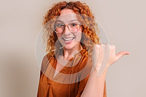 Portrait of young smiling businesswoman with redhead aiming thumb and marketing on white background
