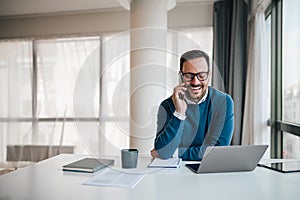 Portrait of young smiling cheerful entrepreneur in casual office making phone call while working