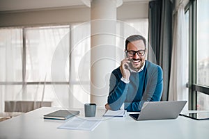 Portrait of young smiling cheerful entrepreneur in casual office making phone call while working photo