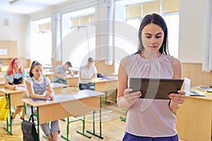 Portrait of young smiling confident female teacher with digital tablet in classroom