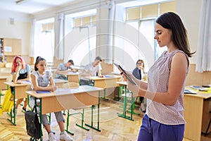 Portrait of young smiling confident female teacher with digital tablet in classroom