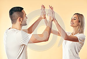 Portrait of young smiling couple giving high five to each other over studio background