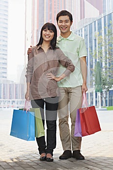 Portrait of young, smiling couple going shopping and holding colorful shopping bags in the street, looking at camera, Beijing, Chi