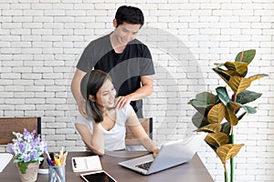 Portrait of young smiling couple working with laptop at home, A man massage shoulder of a girl