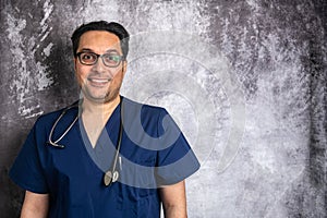 Portrait of a young smiling doctor in glasses with a stethoscope against a gray wall. Space for text