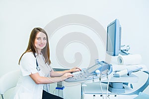 Portrait of young smiling doctor, ultrasound specialist looking at camera and using Ultrasound Scanning Machine for pacient