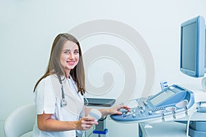 Portrait of young smiling doctor, ultrasound specialist looking at camera and using Ultrasound Scanning Machine for pacient