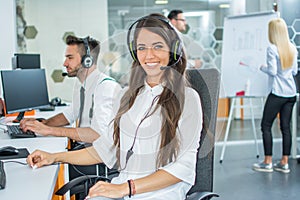 Portrait of young smiling female customer services agent with headset working in call center.