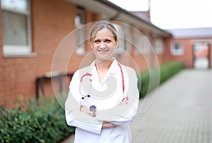 Portrait of young smiling female doctor with red stethoscope near clinic