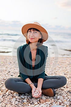 Portrait of a young smiling girl in a hat, sitting on the beach.Beautiful natural beauty woman smiling and laughing, posing for