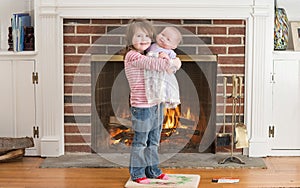 Portrait of a young smiling girl hold a baby doll in front of a fireplace dressed for valentine`s day