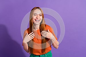 Portrait of young smiling girl in orange t shirt touching chest when someone saying compliments for her isolated on