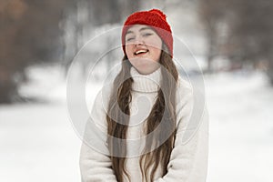 Portrait of a young smiling girl in a red hat on a background of a winter park