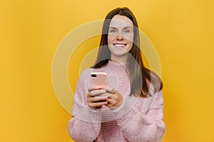 Portrait of young smiling happy cheerful friendly caucasian woman using mobile cell phone chat online, dressed in pink sweater