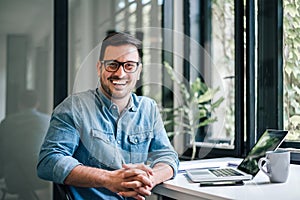 Portrait of young smiling happy handsome successful businessman entrepreneur freelancer working from home office on laptop