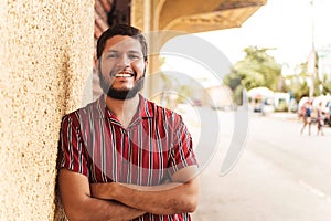 Portrait of a young smiling Hispanic man leaning against the wall, looking at the camera.
