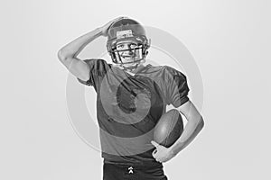 Portrait of young smiling man, american football player posing in uniform and helmet with ball. Black and white