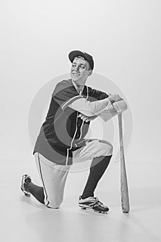 Portrait of young smiling man, baseball player standing on one knee, leaning on bat and posing. Black and white