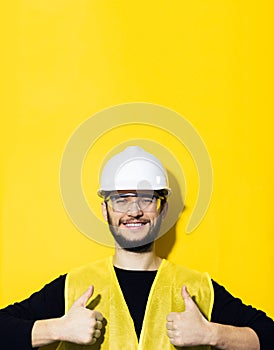 Portrait of young smiling man, builder engineer, showing thumbs up, wearing safety helmet for construction, glasses.