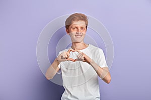 Portrait of a young smiling man doing a heart gesture against a blue background