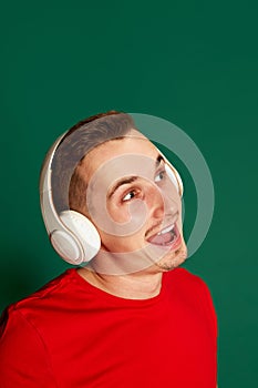 Portrait of young smiling man in red T-shirt posing in headphones isolated over green background. Cheerful. Concept of