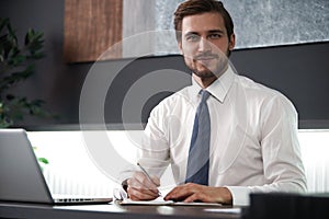 Portrait of young smiling man sitting at his desk in the office.