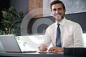 Portrait of young smiling man sitting at his desk in the office.