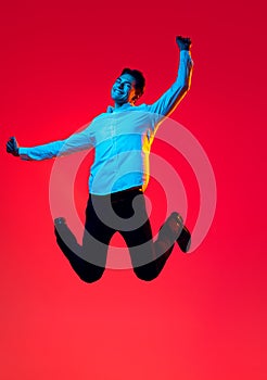 Portrait of young smiling man, student in white shirt cheerfully jumping in excitement isolated over red studio