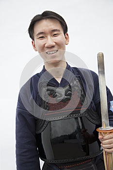 Portrait of young smiling man in traditional Japanese clothing holding a sword, studio shot