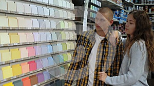 Portrait of young smiling man and woman choosing color for wall painting in a building hypermarket