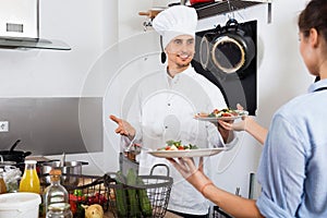 Man cook giving to waitress ready to serve salad