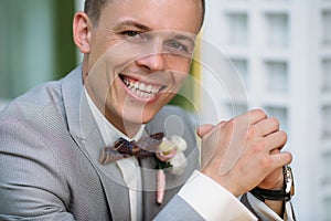 Portrait of a young smiling stylish man in a classic business suit in gray with a white shirt and a bow tie. A young guy