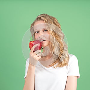 Portrait of young smiling woman bitting red apple againt green wall background. Fresh face