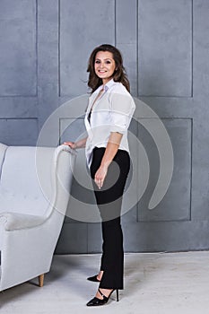 Portrait of a young smiling woman on a gray wall background. A beautiful girl in white shirt and black lingerie stands near a conc