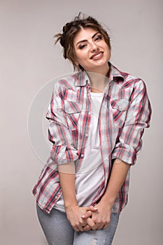 Portrait of a young smiling woman in plaid shirt and white t-shirt, standing over gray wall