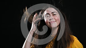 Portrait of a young smiling woman posing on a black background, and her hair from below blows the air. Slow motion.