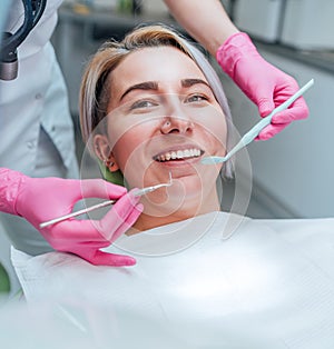 Portrait of young smiling woman sitting in stomatology clinic chair and doctor\'s hands with dental Mouth mirror and Dental