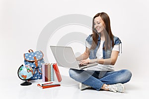 Portrait of young smiling woman student holding using laptop pc computer sitting near globe, backpack, school books