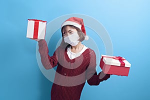 Portrait of young smiling woman in surgical mask wearing red Santa Claus hat isolated blue background studio