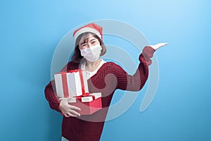 Portrait of young smiling woman in surgical mask wearing red Santa Claus hat isolated blue background studio