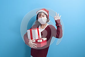 Portrait of young smiling woman in surgical mask wearing red Santa Claus hat isolated blue background studio