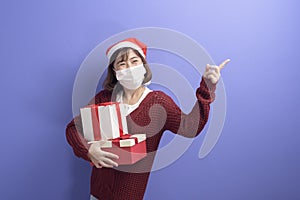 Portrait of young smiling woman in surgical mask wearing red Santa Claus hat isolated blue background studio